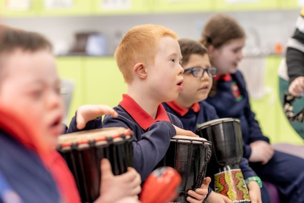A group of children sitting and playing hand drums in a classroom setting at Ceara School, with focused expressions on their faces, enjoying one of the engaging school workshops.