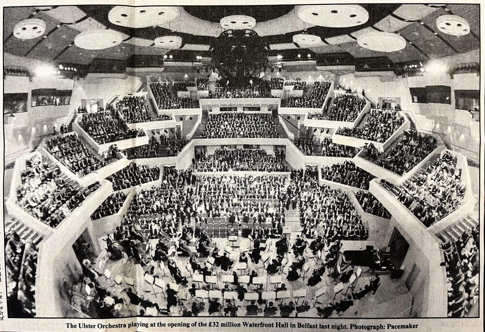 A wide-angle view of the Ulster Orchestra performing on stage before a large audience at the Waterfront Hall in Belfast, where UO Playback has resonated since 1997.