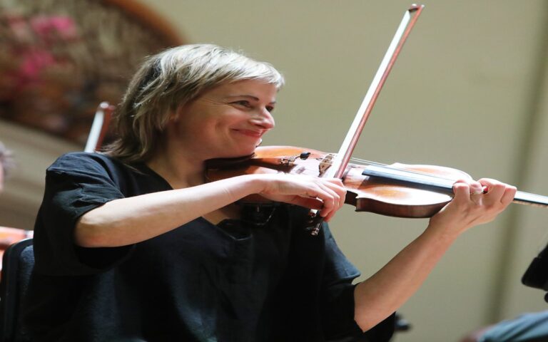 Ioana Petcu-Colan, the New Leader of the Ulster Orchestra, is playing a violin indoors, smiling while performing in a black shirt.