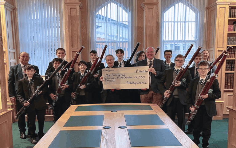 A group of students and adults, some holding bassoons, pose indoors with a large check for £2,000 made out to the Bromyard Symphony for Schools Project.