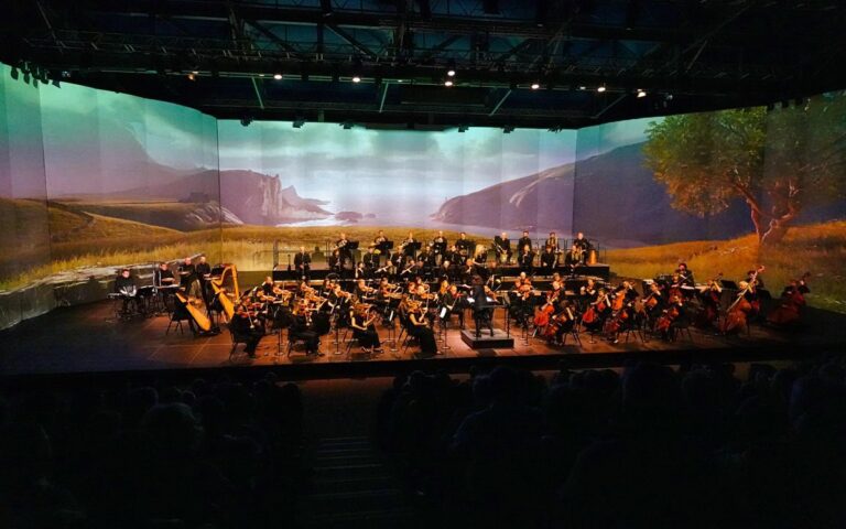 The Ulster Orchestra performs on stage with string, brass, and percussion instruments; a scenic landscape is projected as the backdrop, capturing the vibrant spirit of Festival Berlioz.