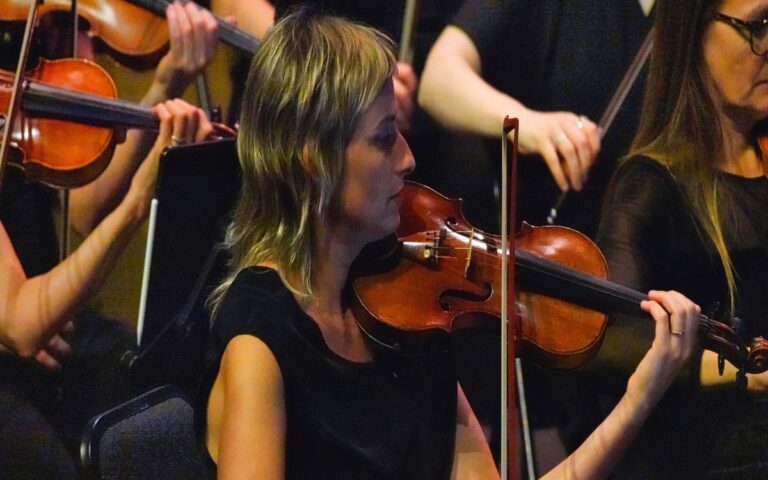 A woman playing the violin in an orchestra, surrounded by other violinists dressed in black, captures a harmonious moment from 2023 in Review.
