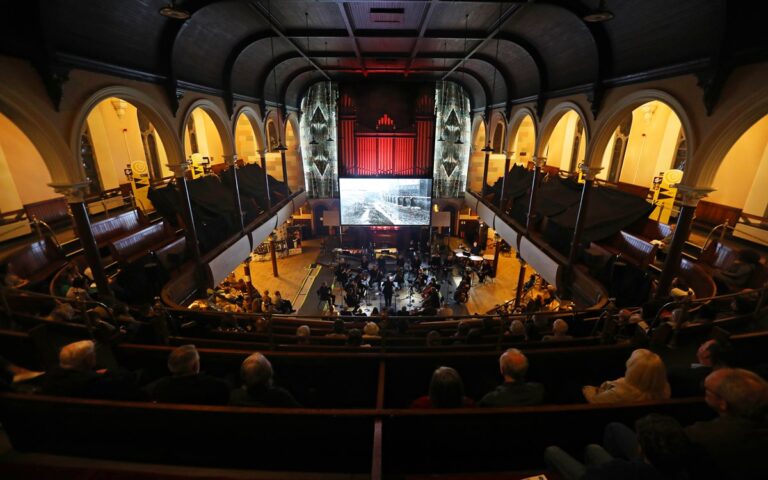 Audience seated in a large church with high ceilings and arched windows, watching the Ulster Orchestra’s performance and a projected image at the front altar area during a Townsend Community event.