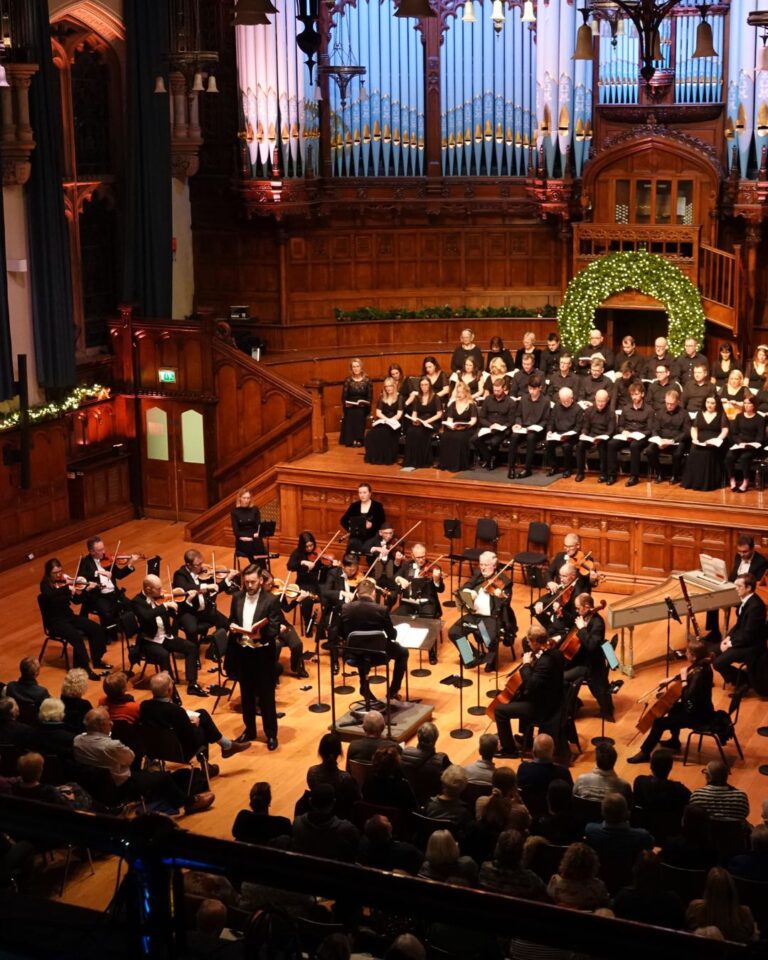 An orchestra and a choir perform in a large hall which is decorated for Christmas.